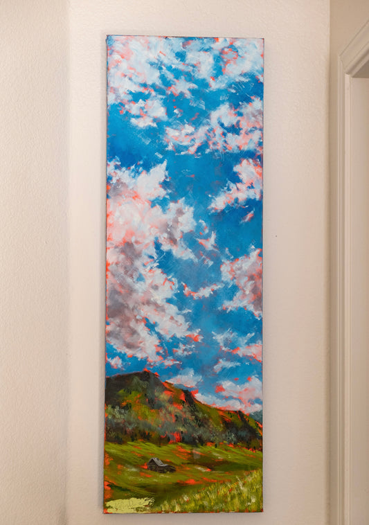 Painting of a landscape with a blue sky and green fields on a beige wall.